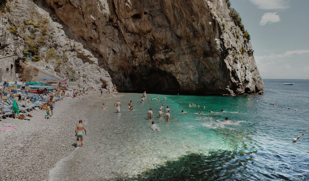 Tourists enjoy bathing on Amalfi coast beach with crystal clear water.