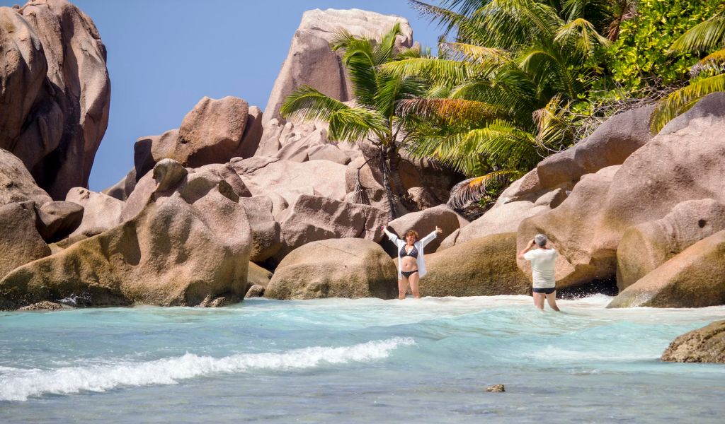A couples enjoy taking a picture at the beach with beautiful rock formations, located in Seychelles.