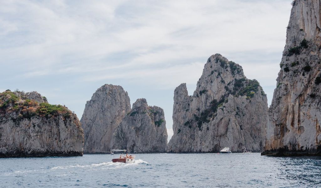Boat sailing at sea surrounded by gray mountains located in Capri.