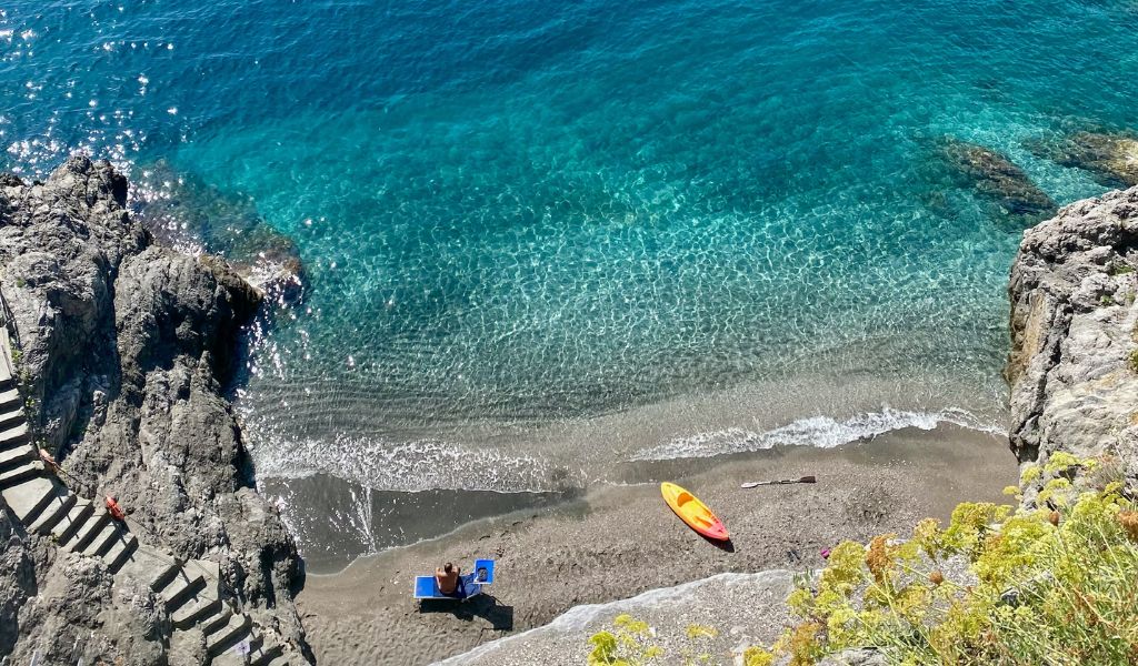 A man sitting and enjoying the view of Maiori beach with crystal clear water.