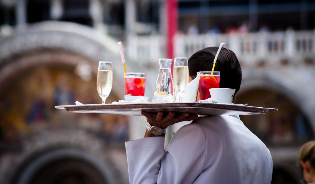 The waiter serves food with the Prosecco and red juices.